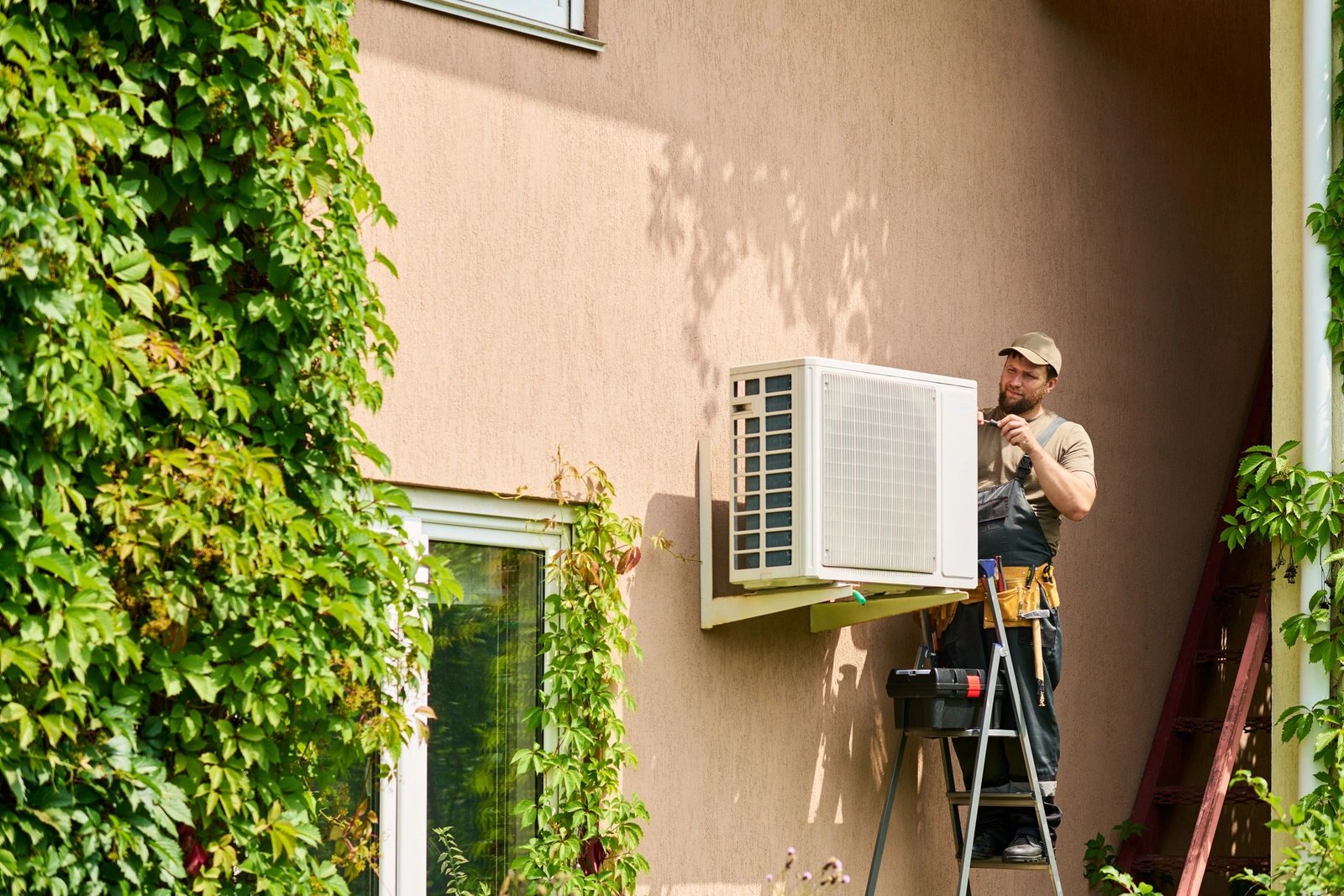 HVAC technician repairing an outdoor air conditioning unit on a ladder